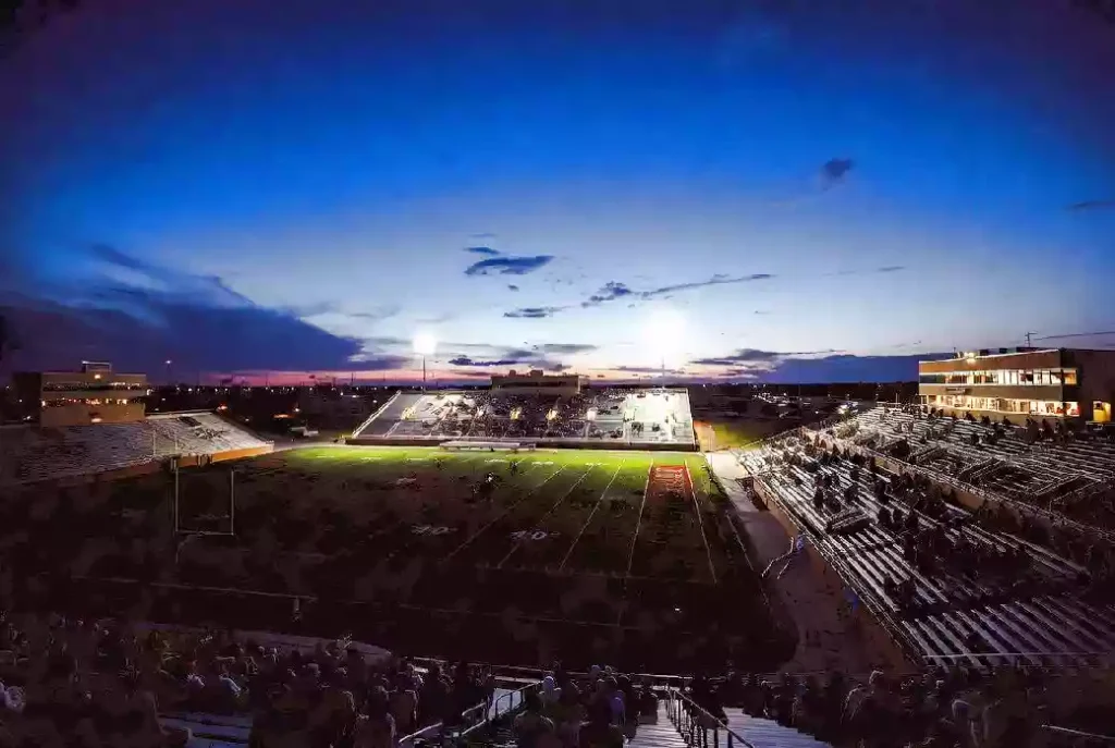 Wide view of a high school football stadium at dusk under stadium lights in Norman Oklahoma