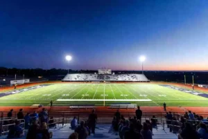 Wide view of a high school football stadium at dusk under stadium lights in central Oklahoma