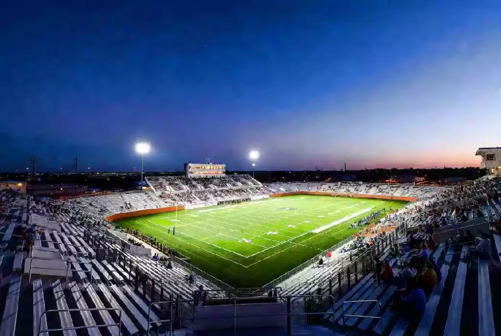 Wide view of a high school football stadium at dusk under stadium lights in McAlester Oklahoma