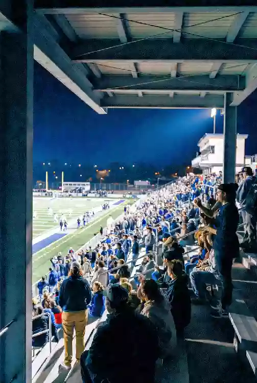Vertical photo of fans watching a high school football game under the lights in Broken Arrow