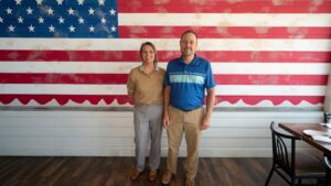 Amber Mordecai, new Executive Director of the Henryetta Chamber of Commerce, with Chamber President Kenny Wilson in front of an American flag wall