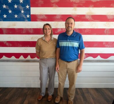 Amber Mordecai, new Executive Director of the Henryetta Chamber of Commerce, with Chamber President Kenny Wilson in front of an American flag wall