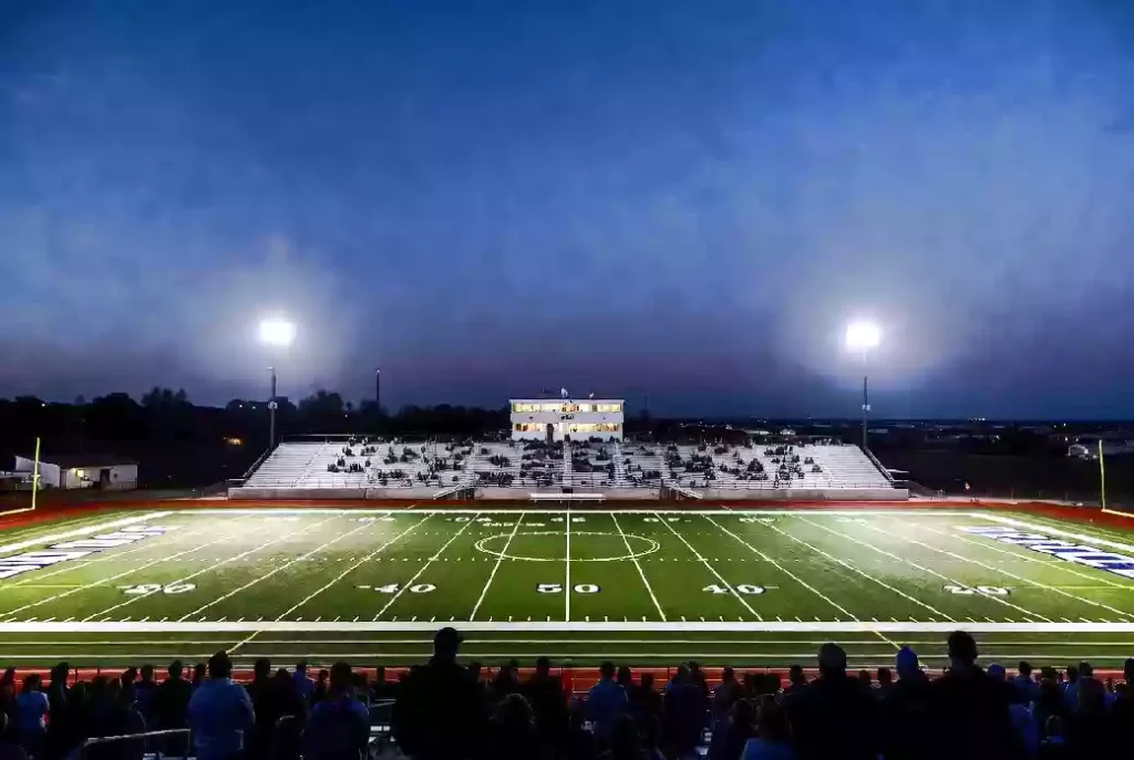 Wide view of a high school football stadium at dusk under stadium lights in Okmulgee Oklahoma