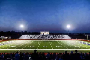 Wide view of a high school football stadium at dusk under stadium lights in Okmulgee Oklahoma