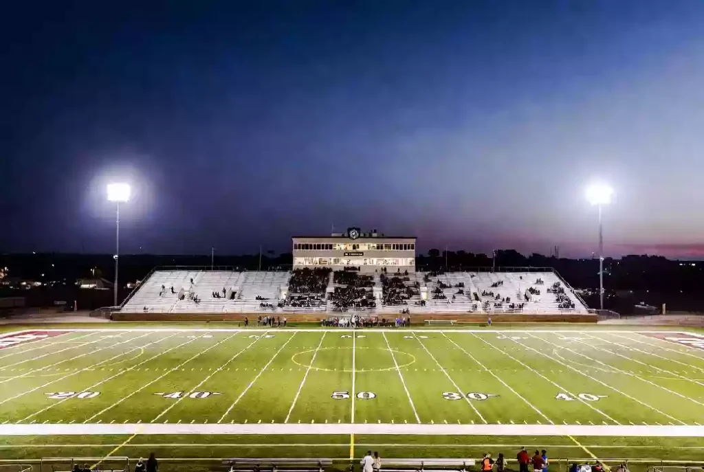 Wide view of a high school football stadium at dusk under stadium lights in Stillwater Oklahoma