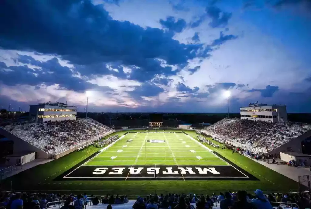 Wide view of a high school football stadium at dusk under stadium lights in Mustang Oklahoma