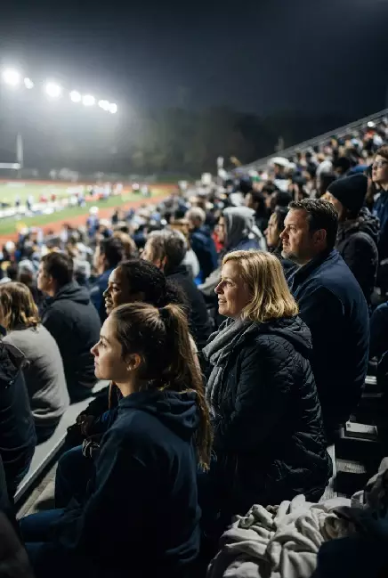 Vertical photo of fans watching a high school football game under the lights in Bartlesville