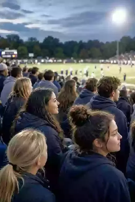 Vertical photo of fans watching a high school football game under the lights in Tahlequah