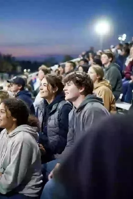 Vertical photo of fans watching a high school football game under the lights in Ardmore