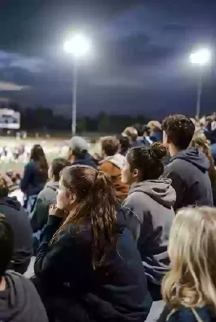 Vertical photo of fans watching a high school football game under the lights in Duncan