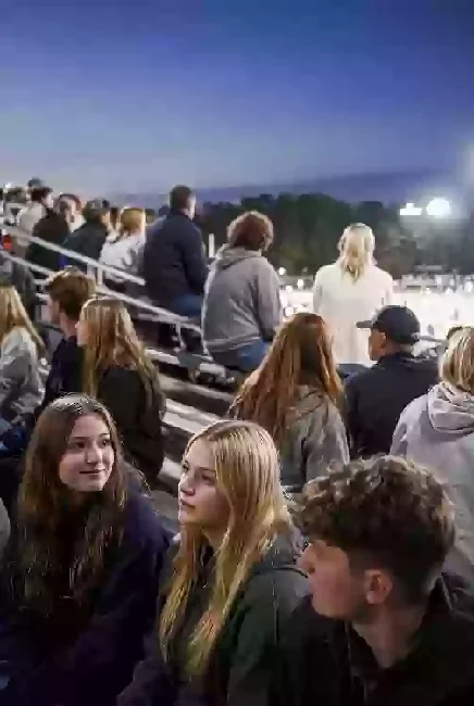 Vertical photo of fans watching a high school football game under the lights in Custer County
