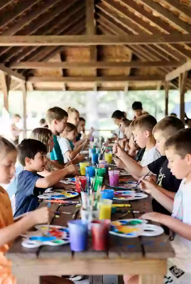 Children painting at long table under pavilion during summer art camp