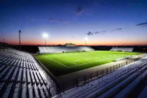 Wide view of a high school football stadium at dusk under stadium lights in Muskogee Oklahoma