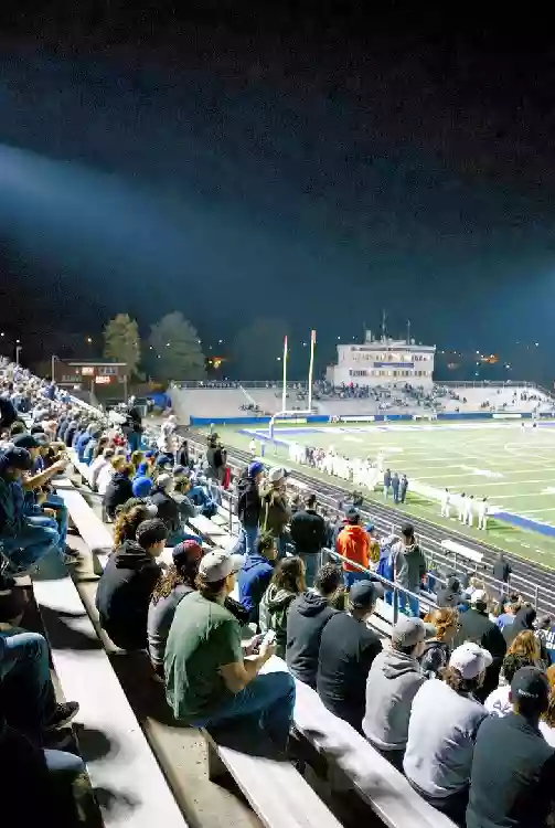 Vertical photo of fans watching a high school football game under the lights in Edmond